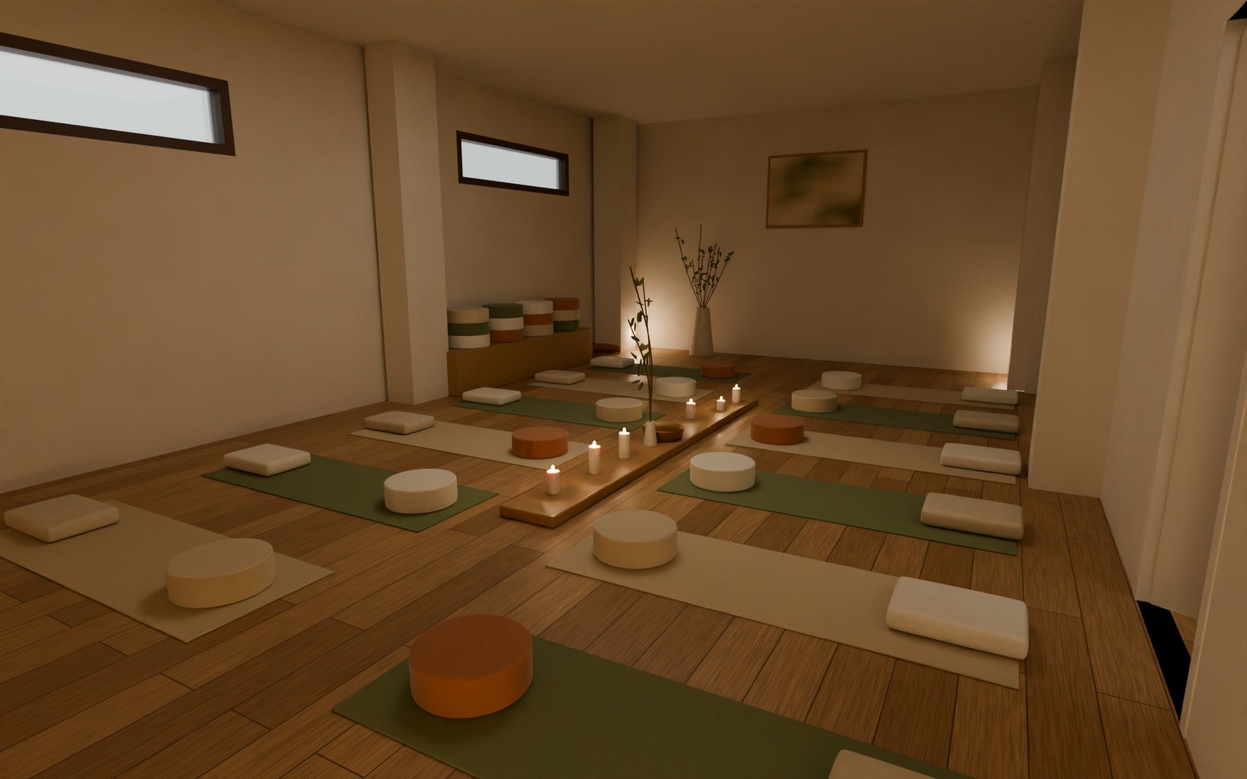 Sala de grupo preparada para una práctica: dos filas de esterillas con zafus y mantas, velas en el pasillo y luz cálida.